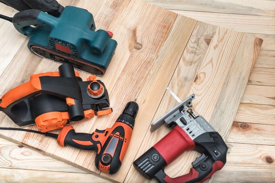 An assortment of power tools and handplanes and power planers resting on a wooden board.